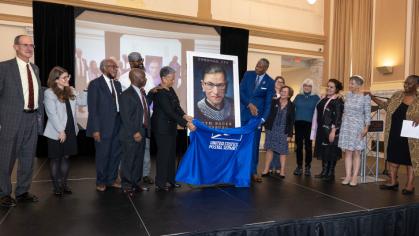 people standing by a portrait of Ruth Bader Ginsburg stamp