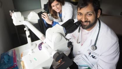 man in a lab coat next to a microscope with a woman looking on
